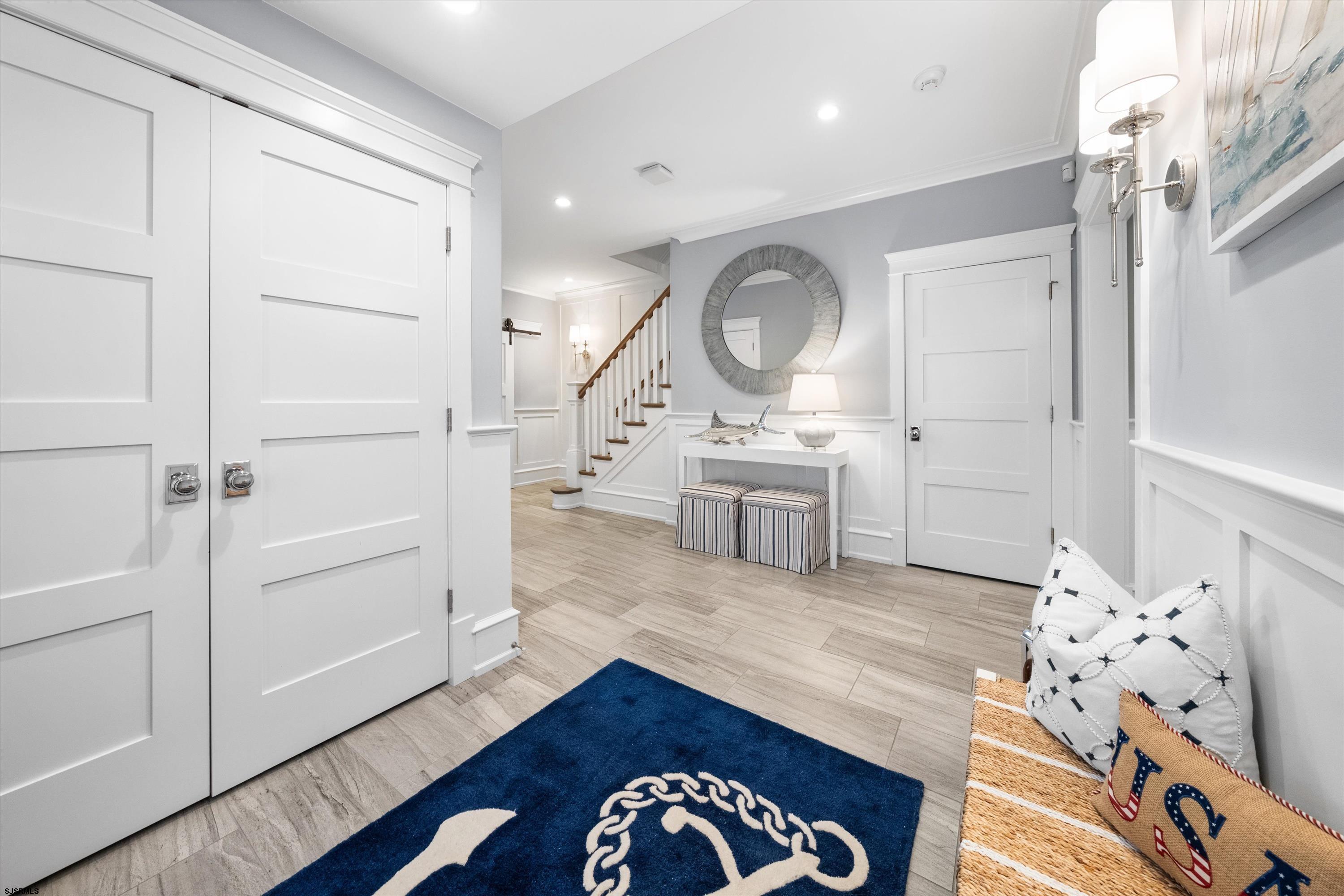 Furnished entry foyer with a blue nautical rug, round mirror, console table, and staircase.