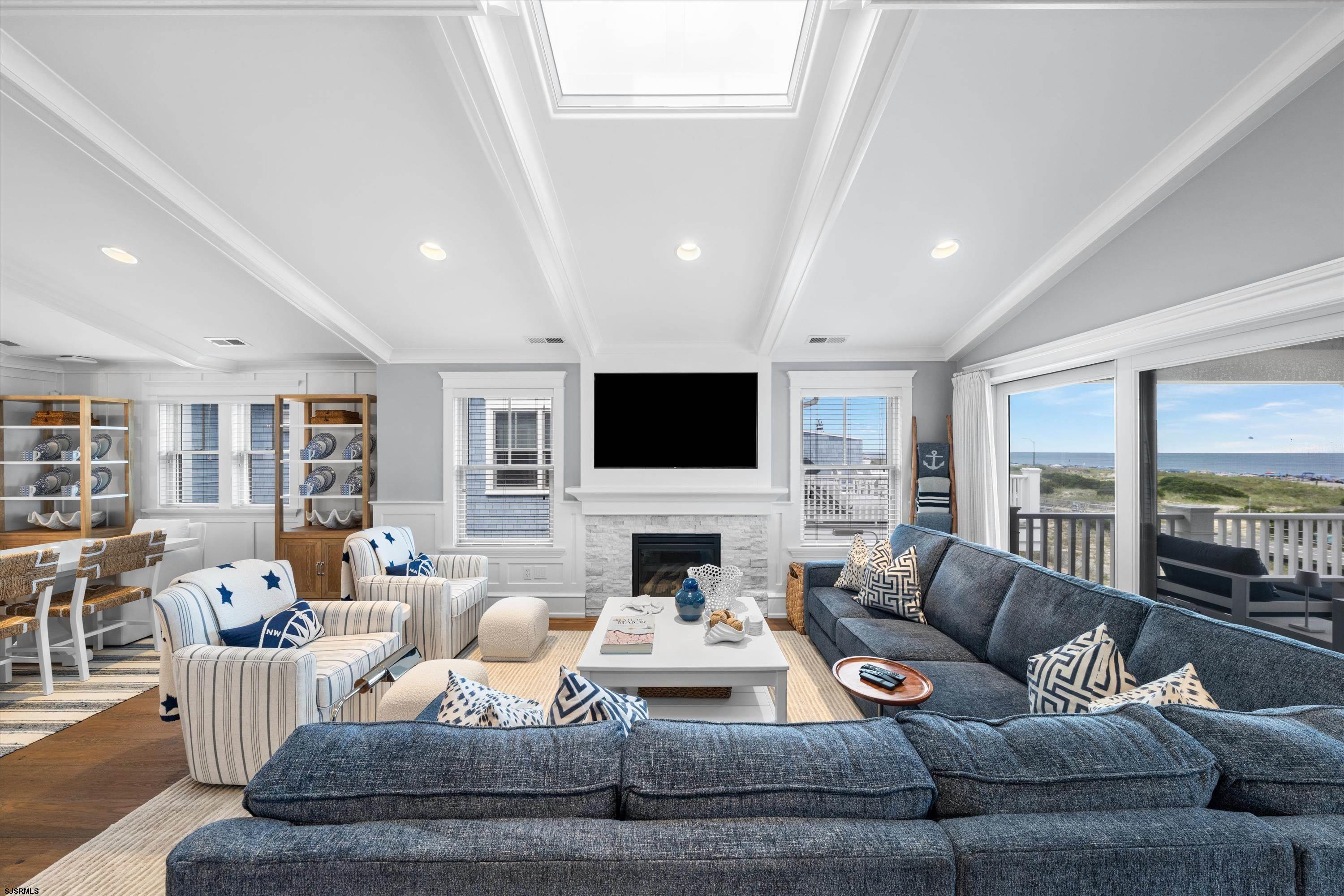 Coastal living room with a stone fireplace, blue seating, and sliding doors overlooking the ocean.