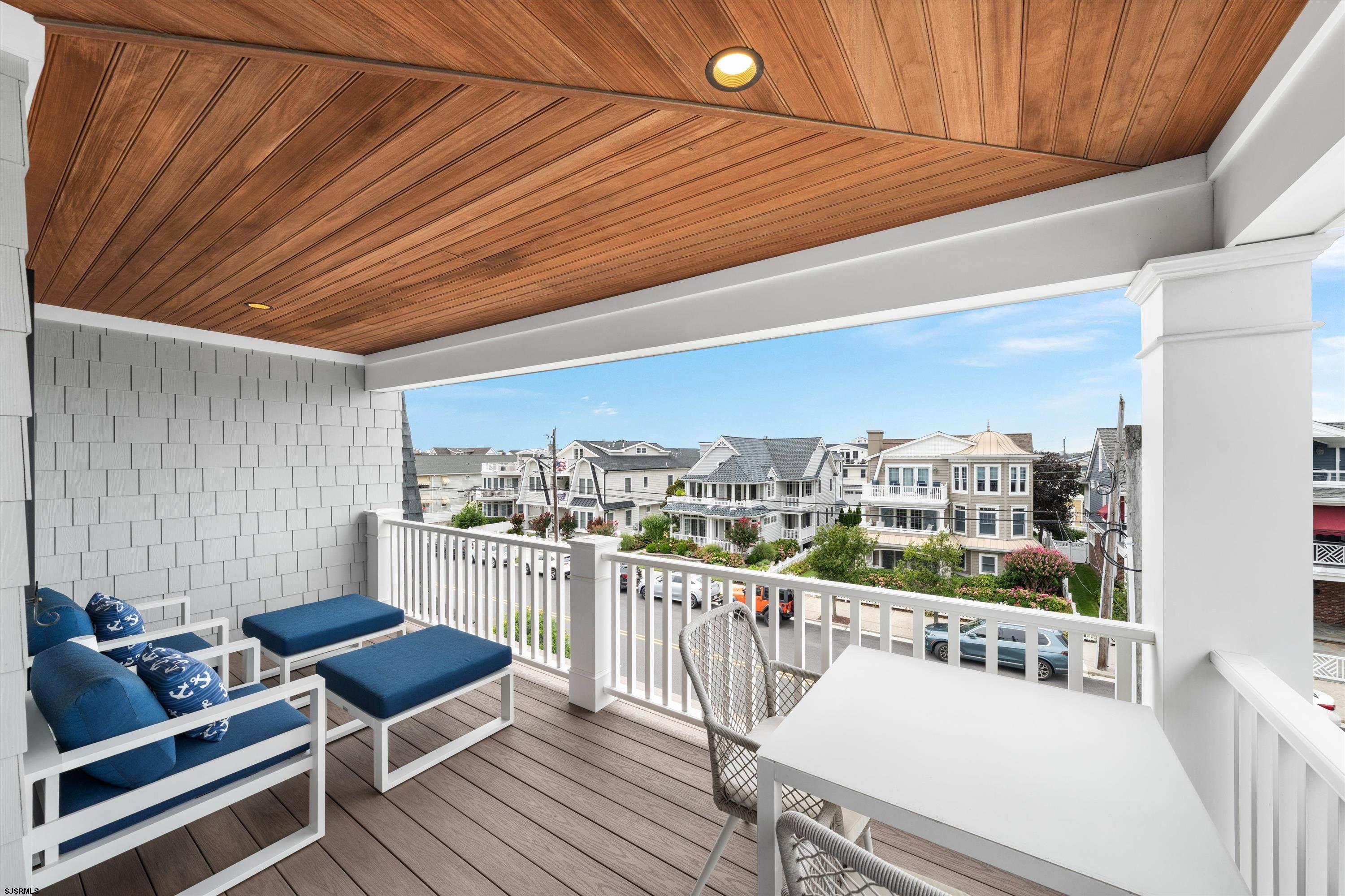 Covered balcony with blue-cushioned seating and a wood ceiling overlooking a residential street.