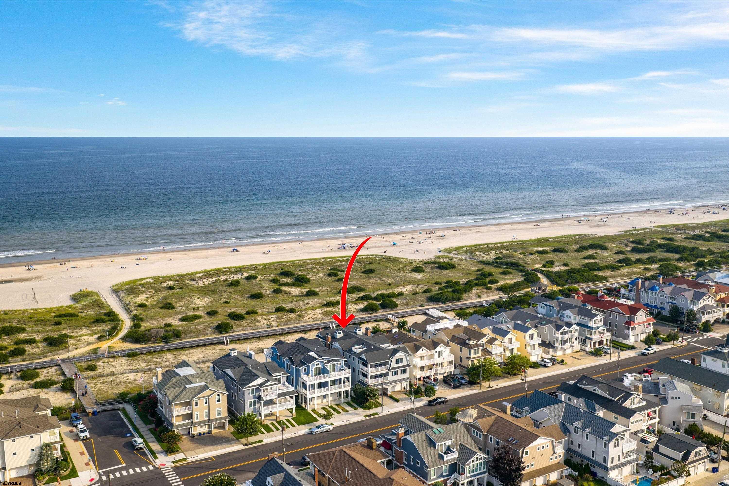 Aerial view of coastal homes beside a sandy beach, with a red arrow marking one house.