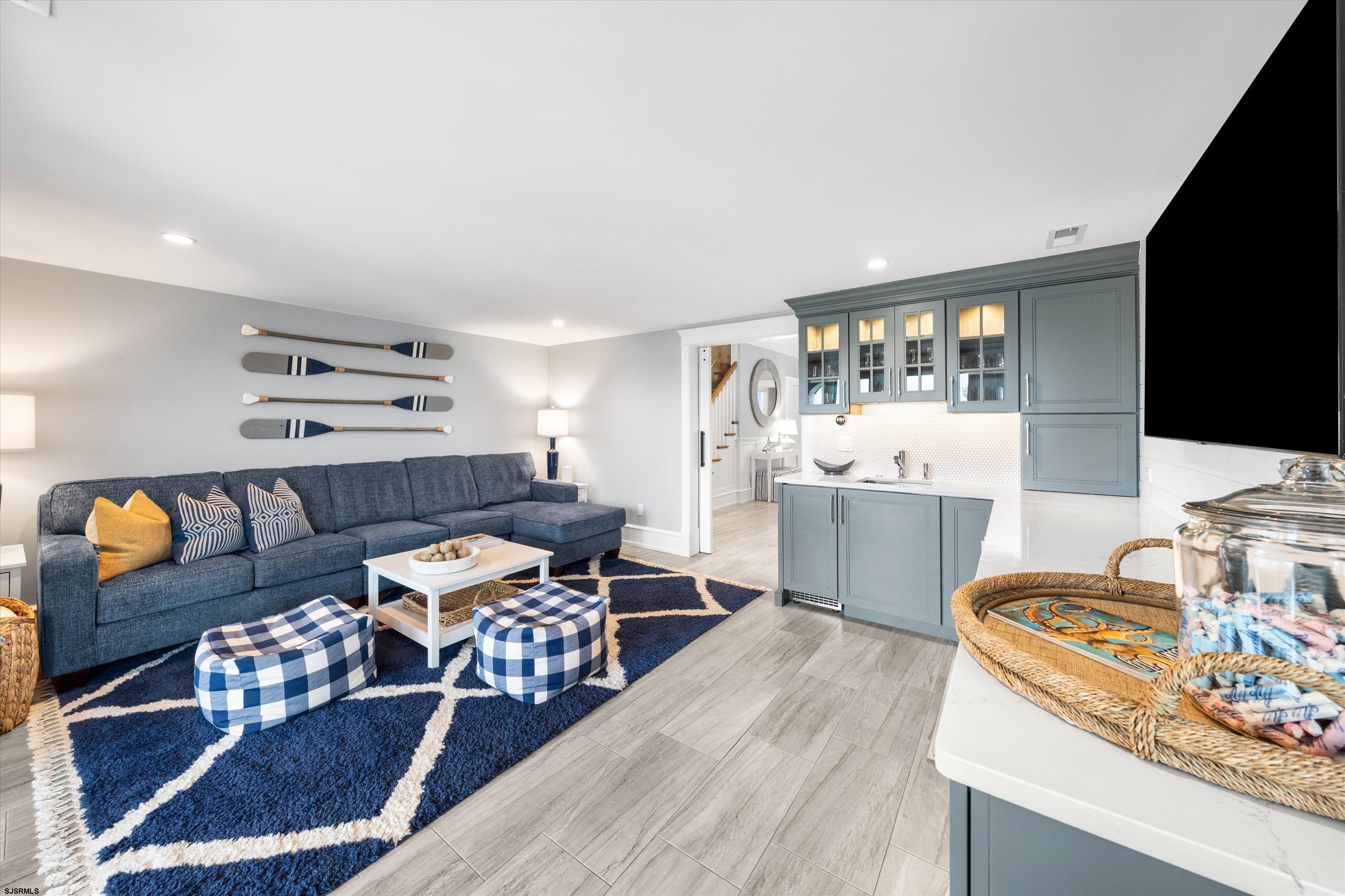 Staged living room with blue sectional and rug beside a blue-gray kitchenette.