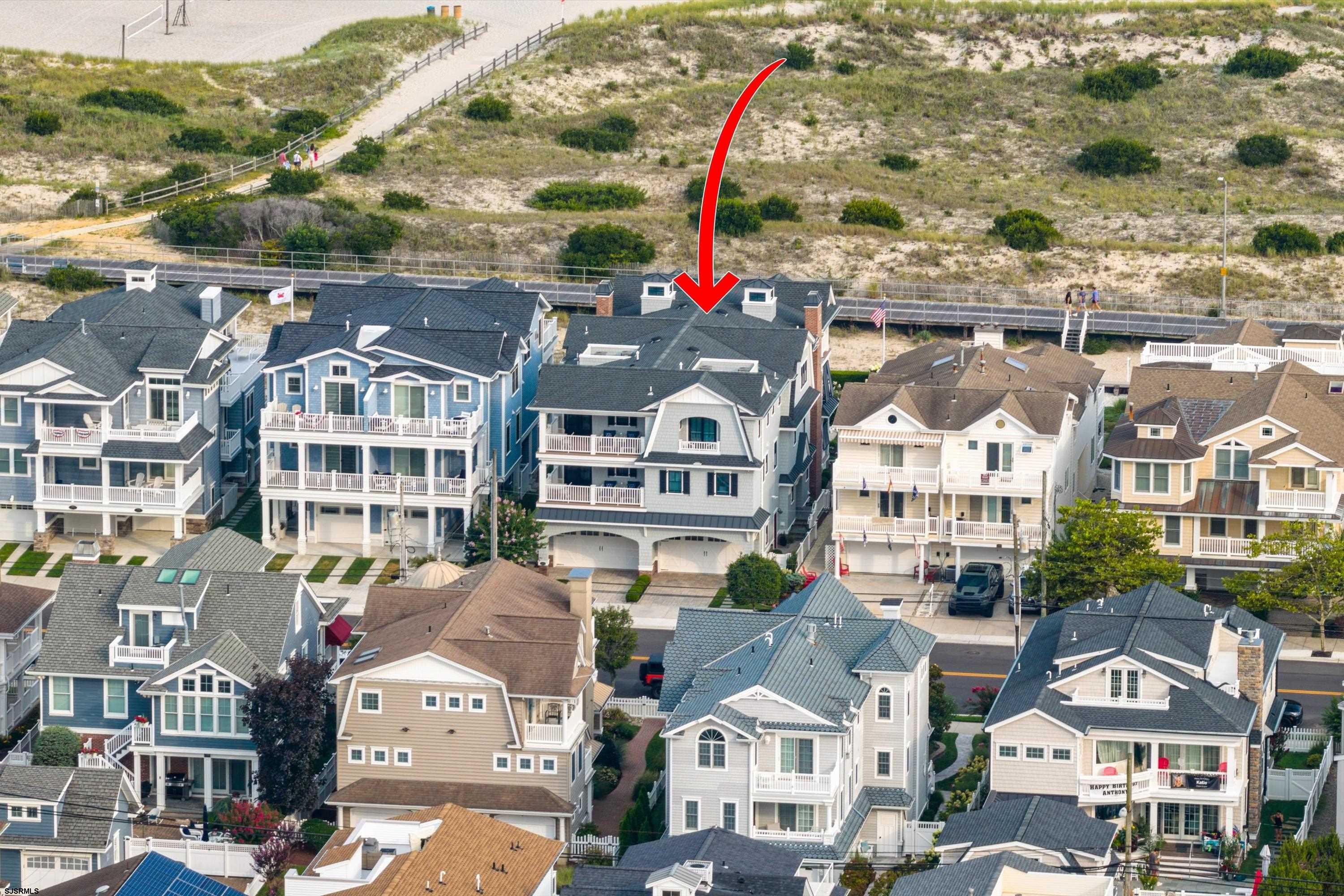 Aerial view of the marked coastal home with balconies beside a sandy dune and boardwalk.