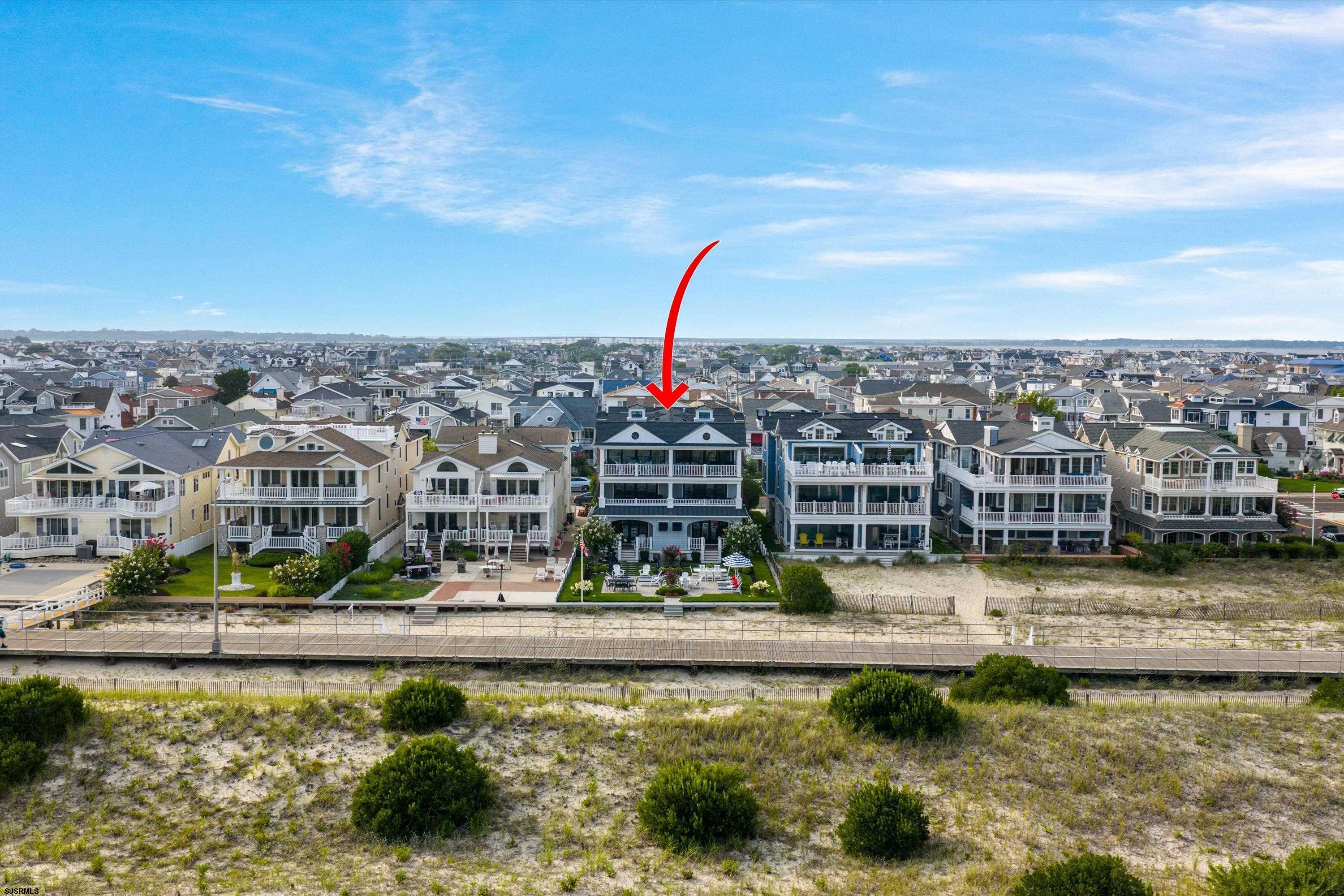 Aerial view of a coastal home marked by a red arrow, behind dunes and a boardwalk.