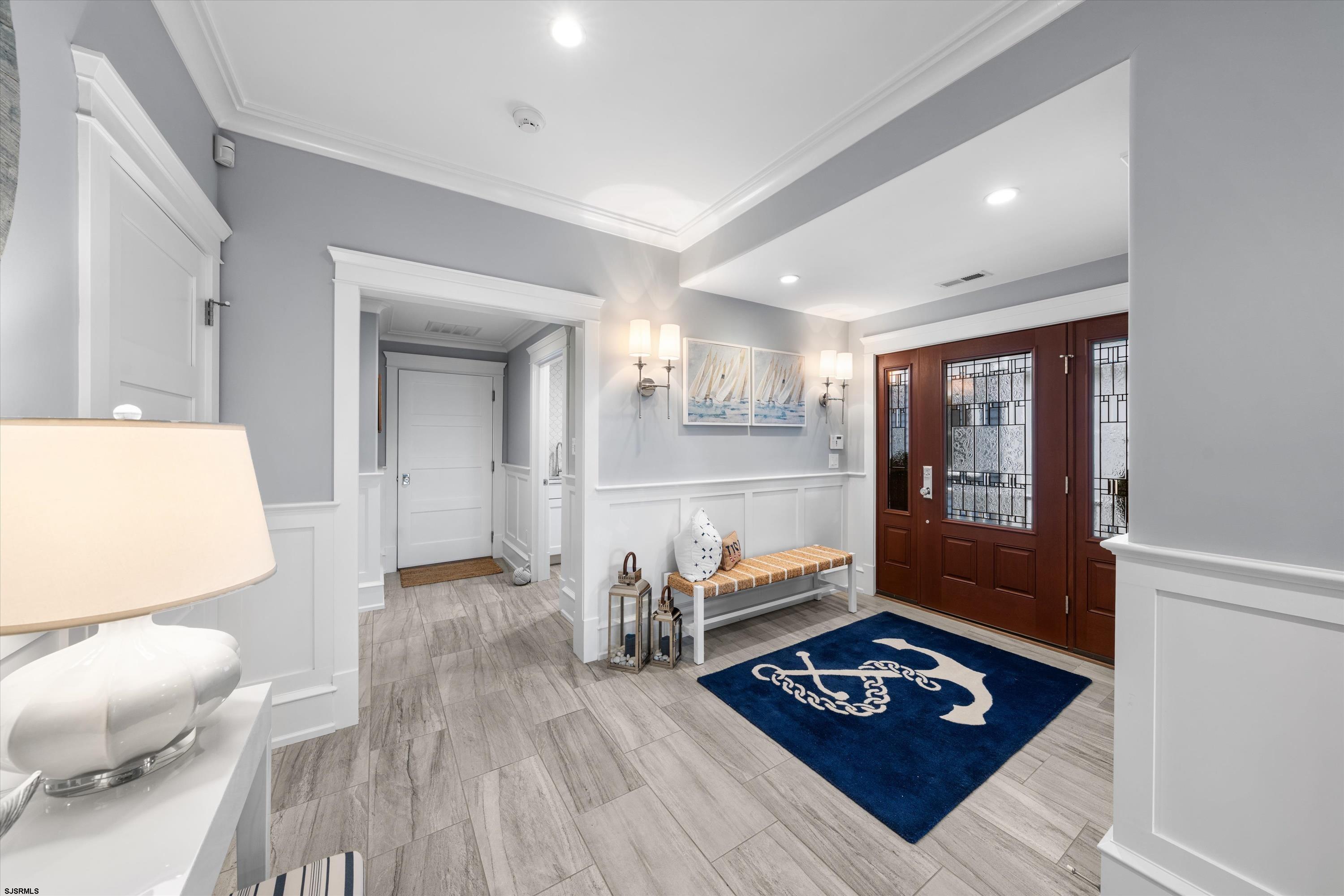 Entry foyer with a dark wood glass-panel door, cushioned bench, and blue anchor rug.