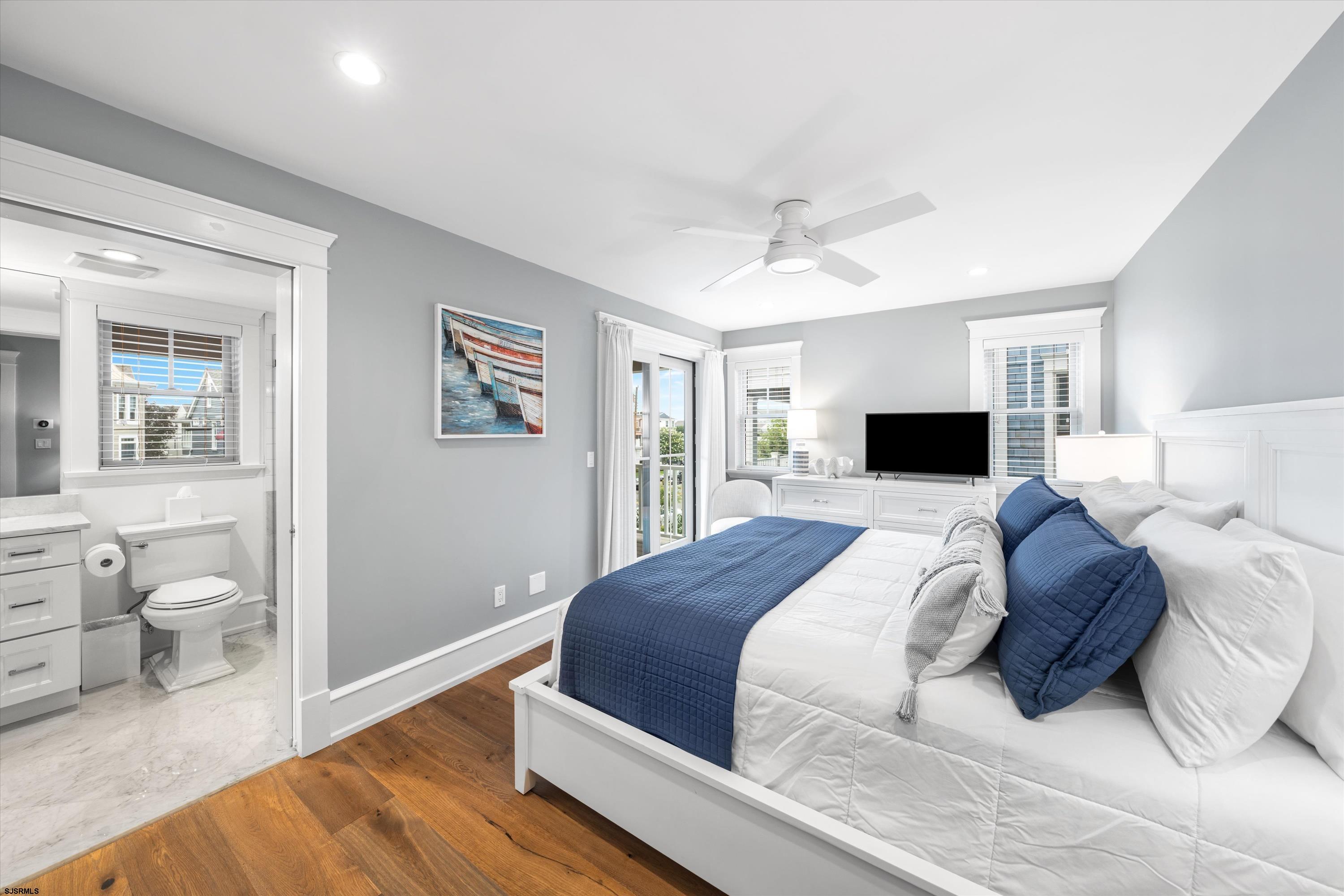 Furnished bedroom with navy bedding, hardwood floors, and an adjoining bathroom.
