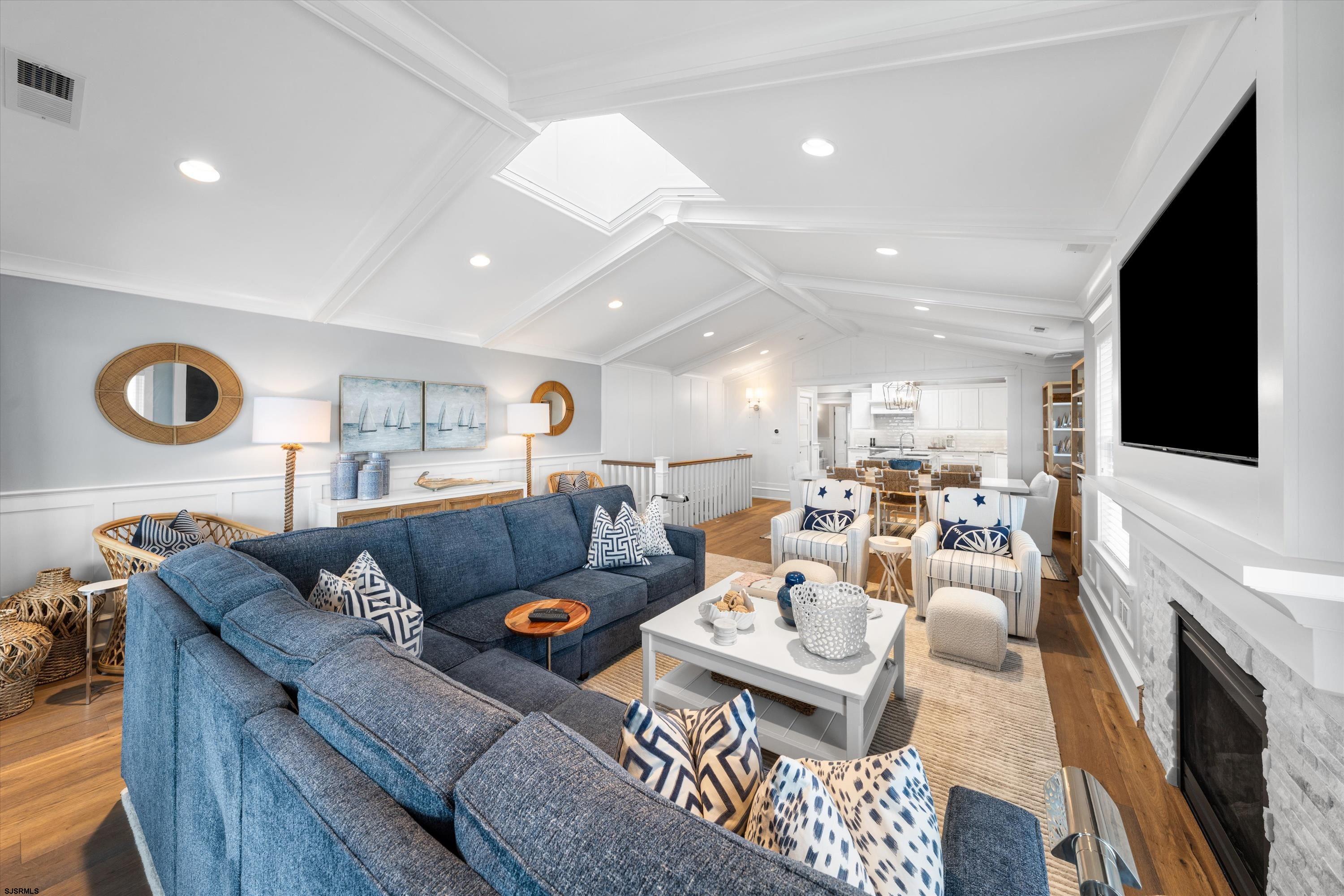 Staged living room with a blue sectional, vaulted ceiling, stone fireplace, and open kitchen beyond.