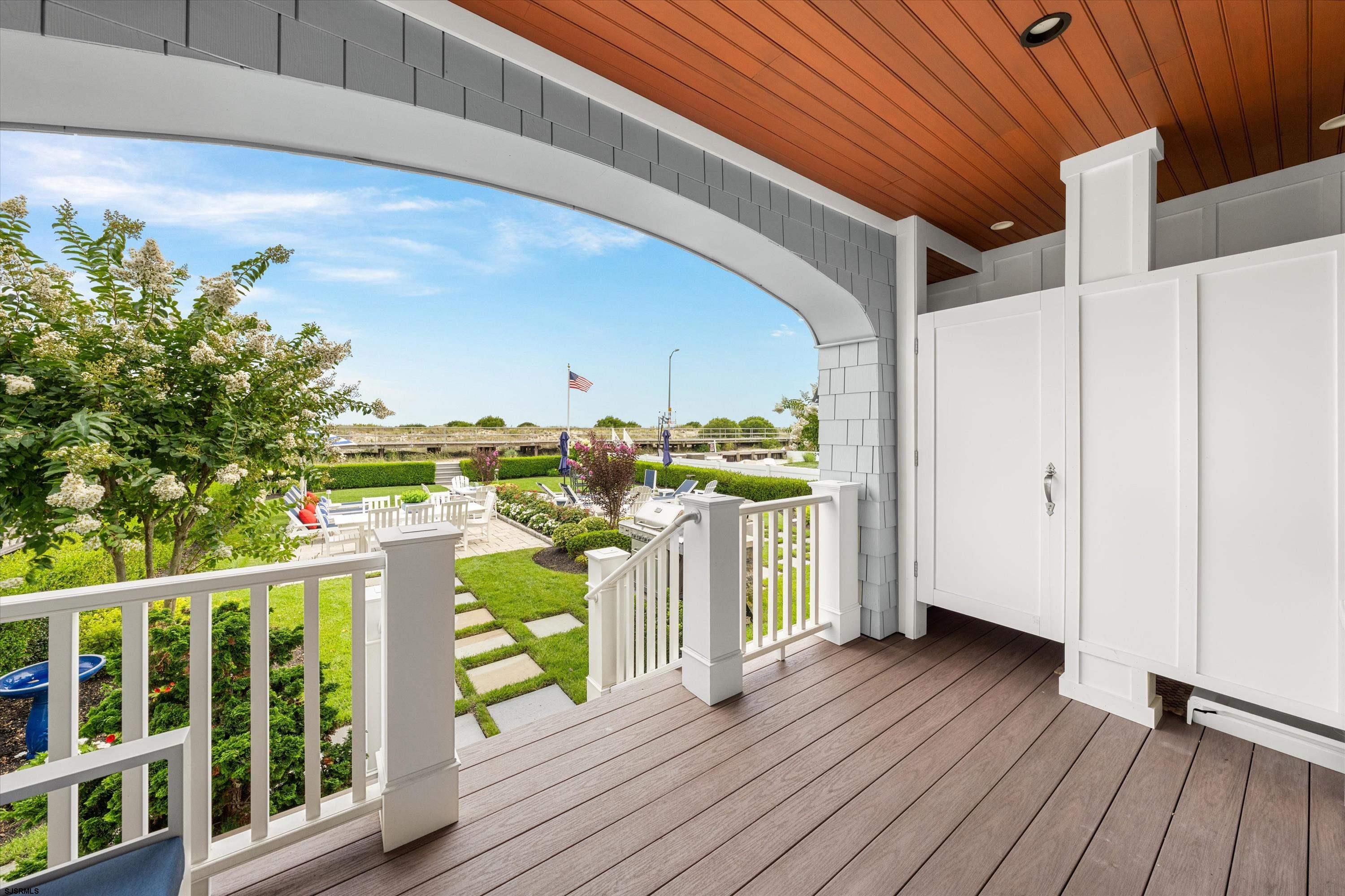 Covered porch overlooking landscaped gardens and outdoor seating, with white railings and a wood-paneled ceiling.