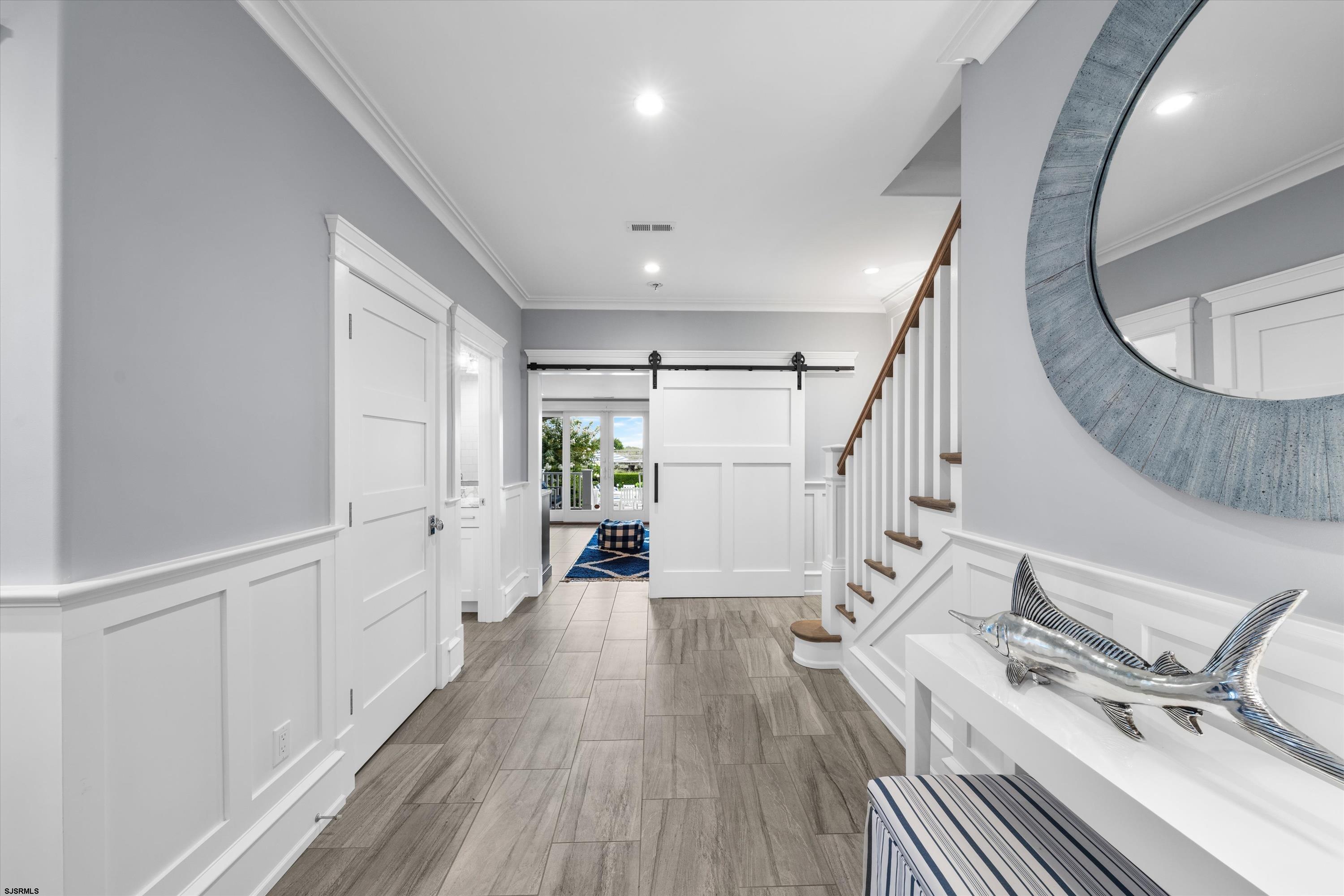 Entry hall with gray tile floors, paneled walls, staircase, and a sliding barn door opening to the living area.