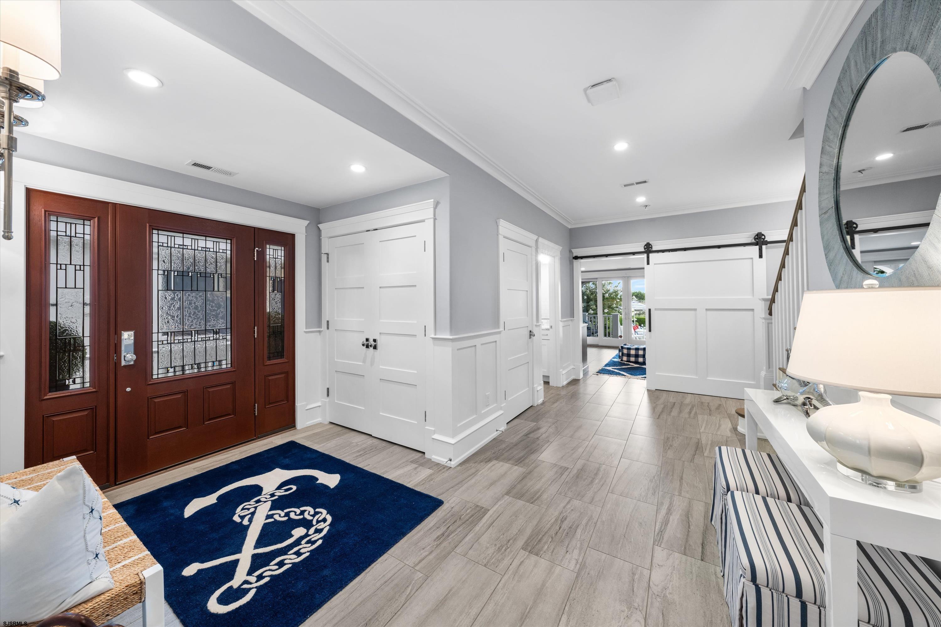 Entry hall with a leaded-glass front door, navy anchor rug, and white barn door.