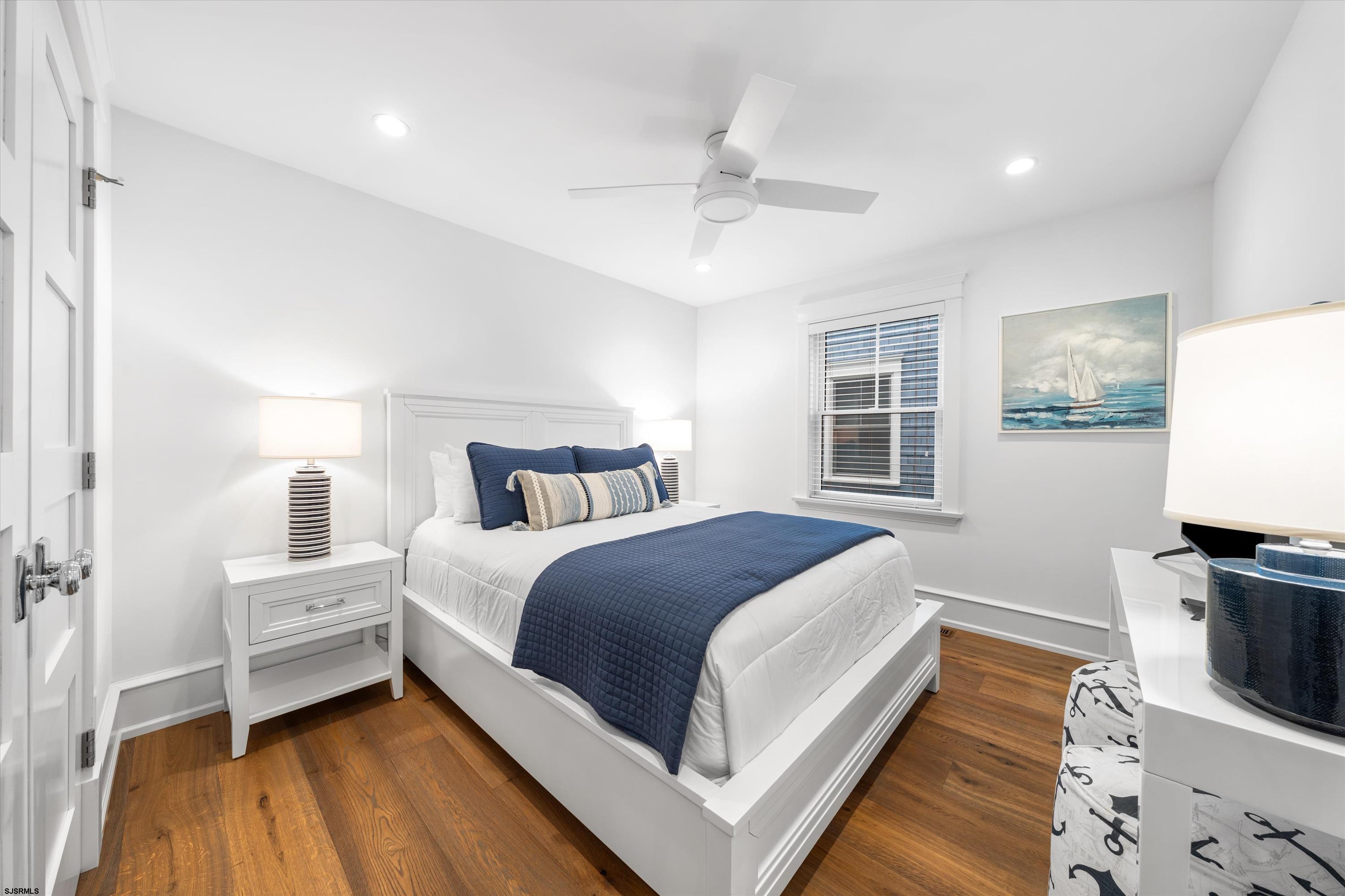 Staged bedroom with a white bed, navy bedding, hardwood floors, and sailboat artwork.