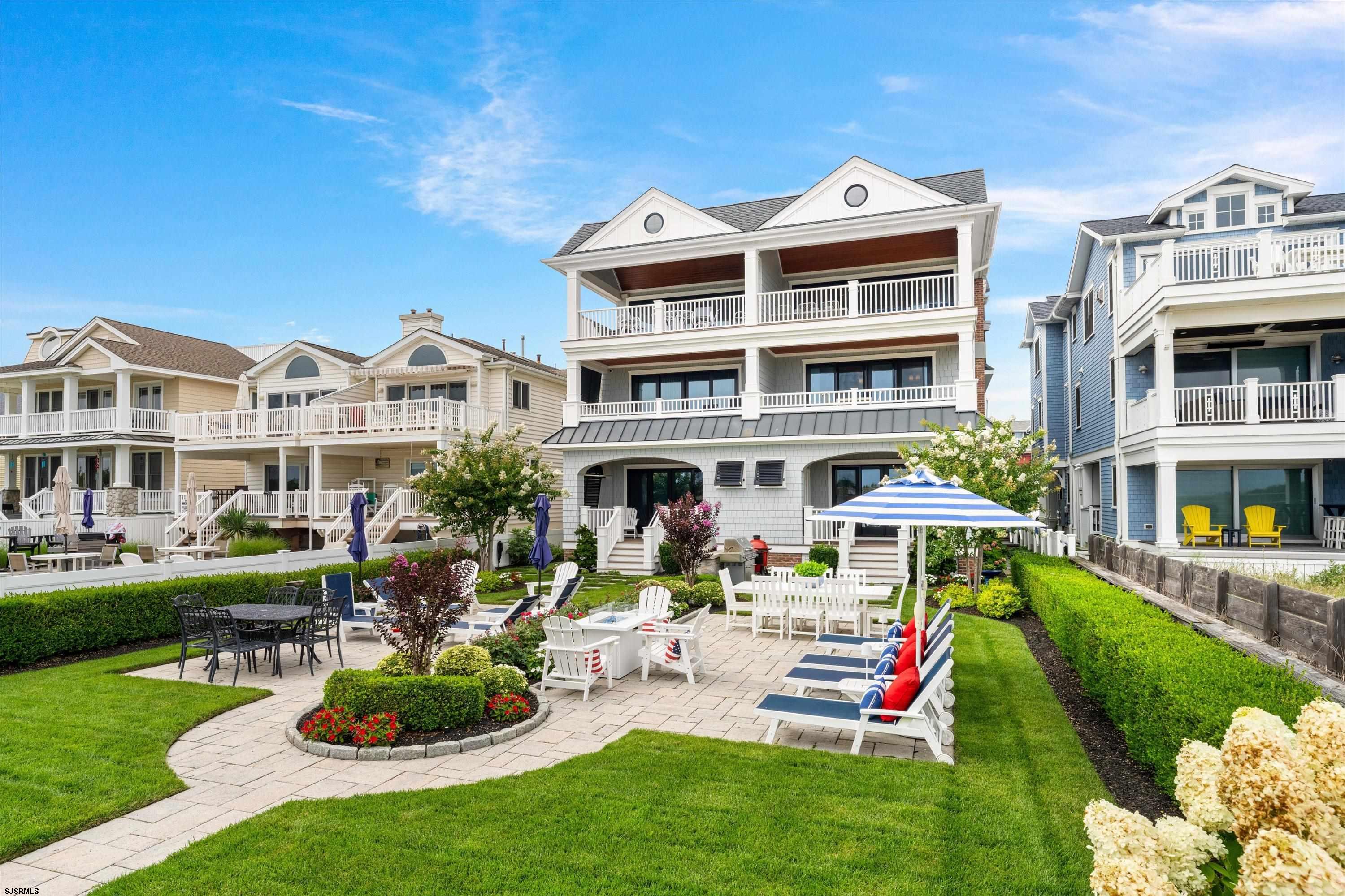 White coastal home with stacked balconies overlooks a landscaped courtyard patio with outdoor dining and lounge seating.