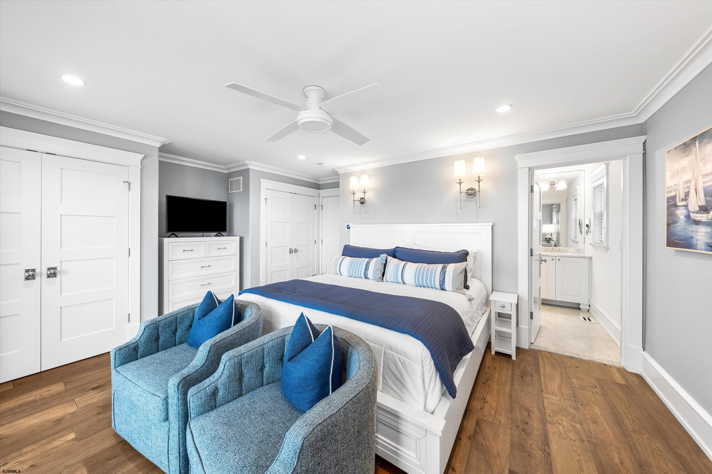 Bedroom with blue-and-white bedding, two blue armchairs, and an open doorway to the ensuite bathroom.
