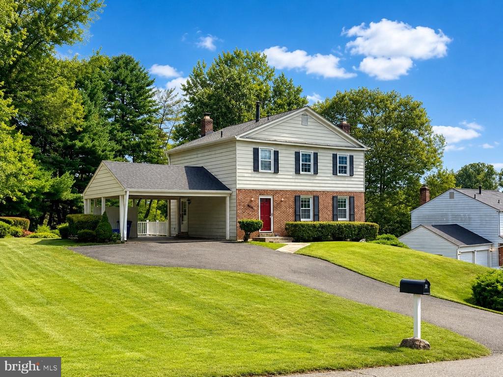 Two-story home with brick and beige siding, red front door, covered carport, and sloping lawn.