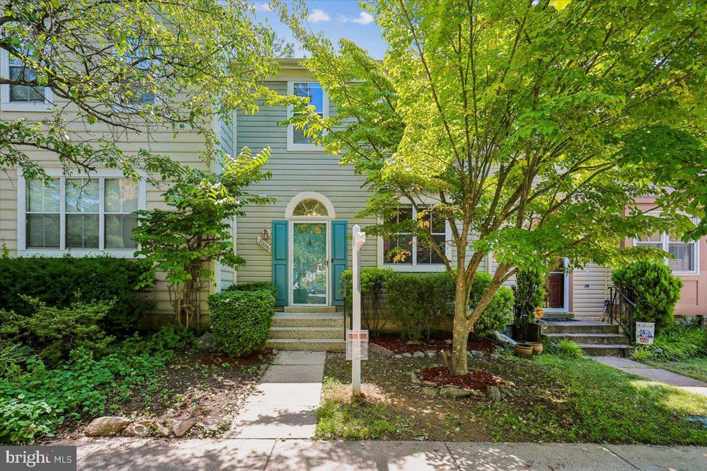 Townhouse exterior with a turquoise front door, front steps, and leafy trees.
