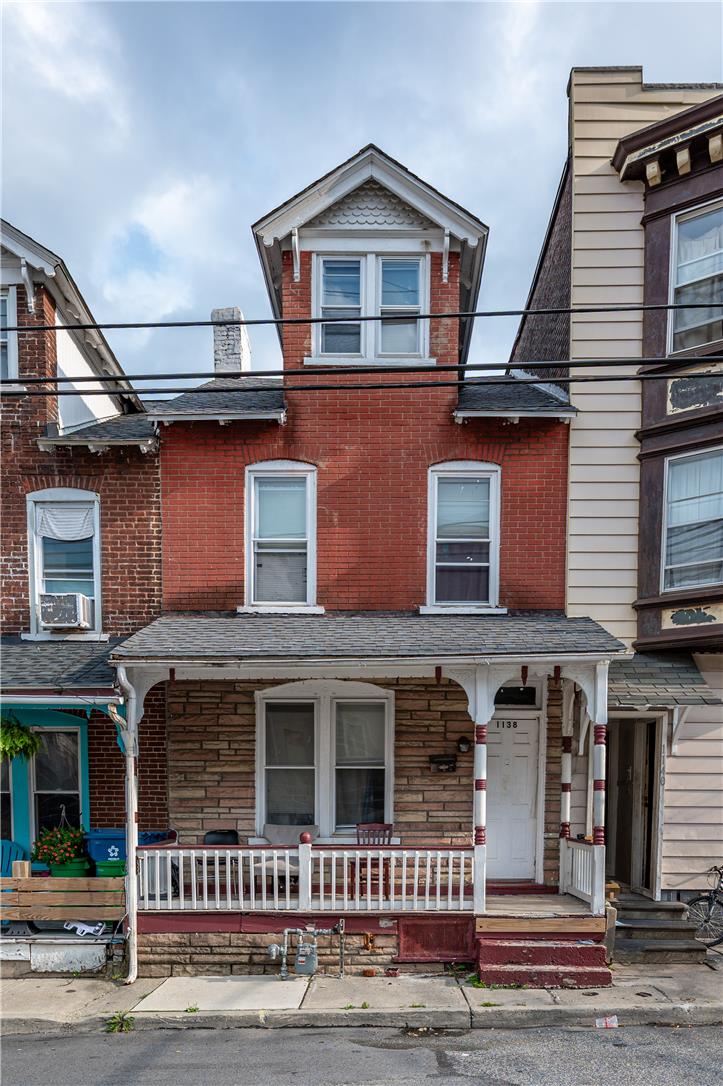 Red-brick rowhouse with a white-railed porch, peaked dormer, and neighboring homes.