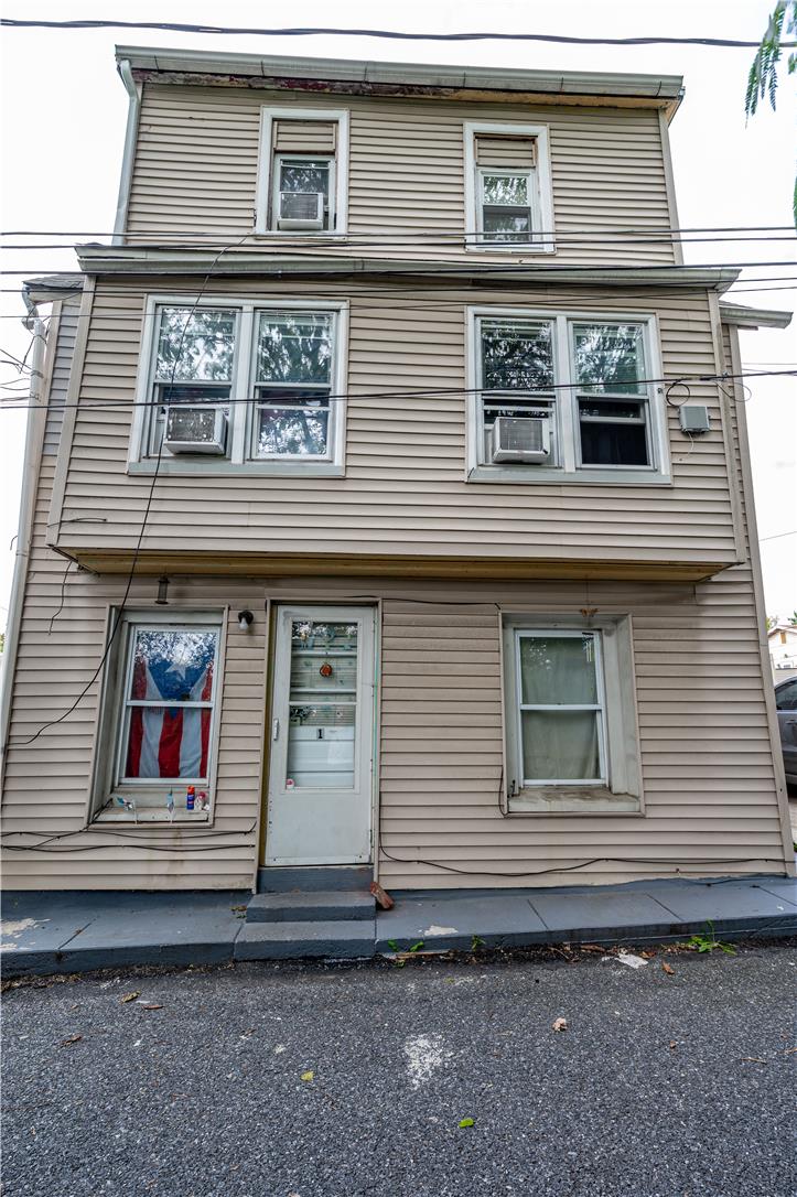 Three-story beige-sided house with a central entrance, window air conditioners, and an American flag in a window.