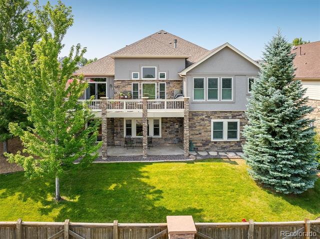 Rear exterior of a two-story stone-and-stucco home with raised deck, fenced lawn, and mature trees.