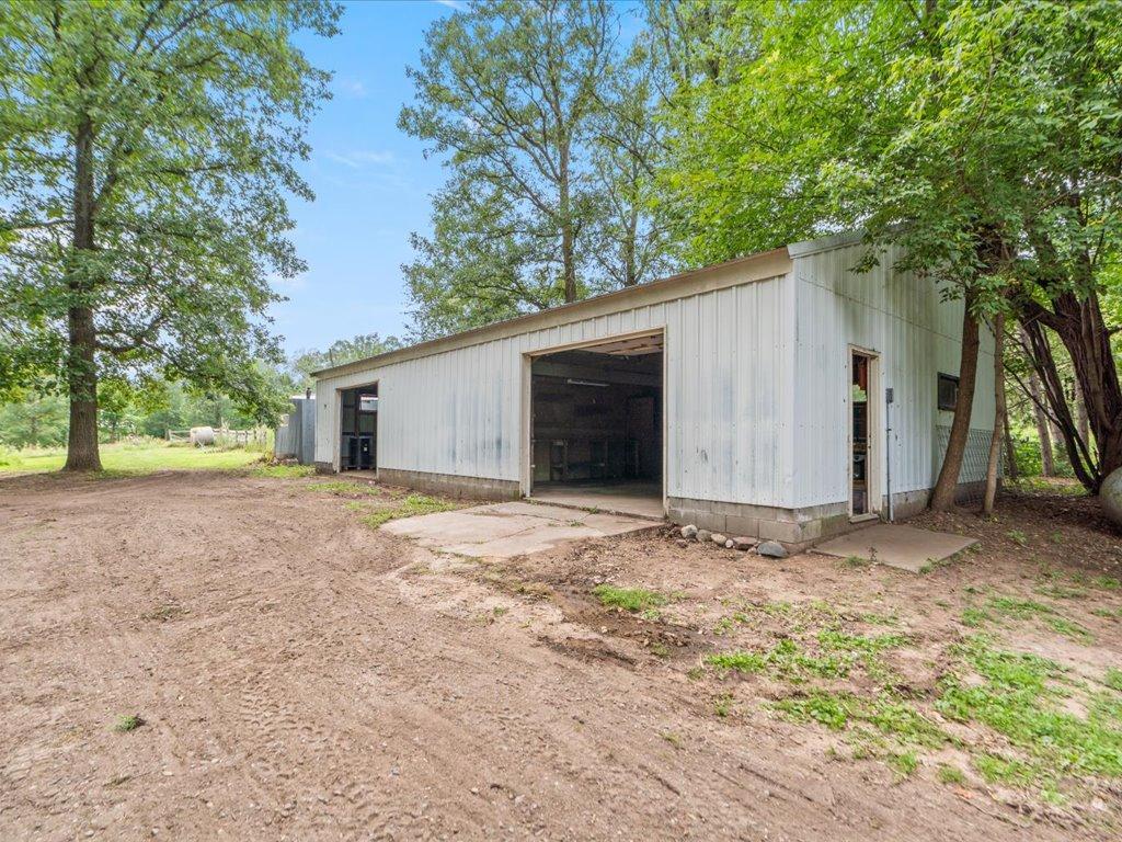 White metal workshop with a wide open garage bay, surrounded by mature trees.