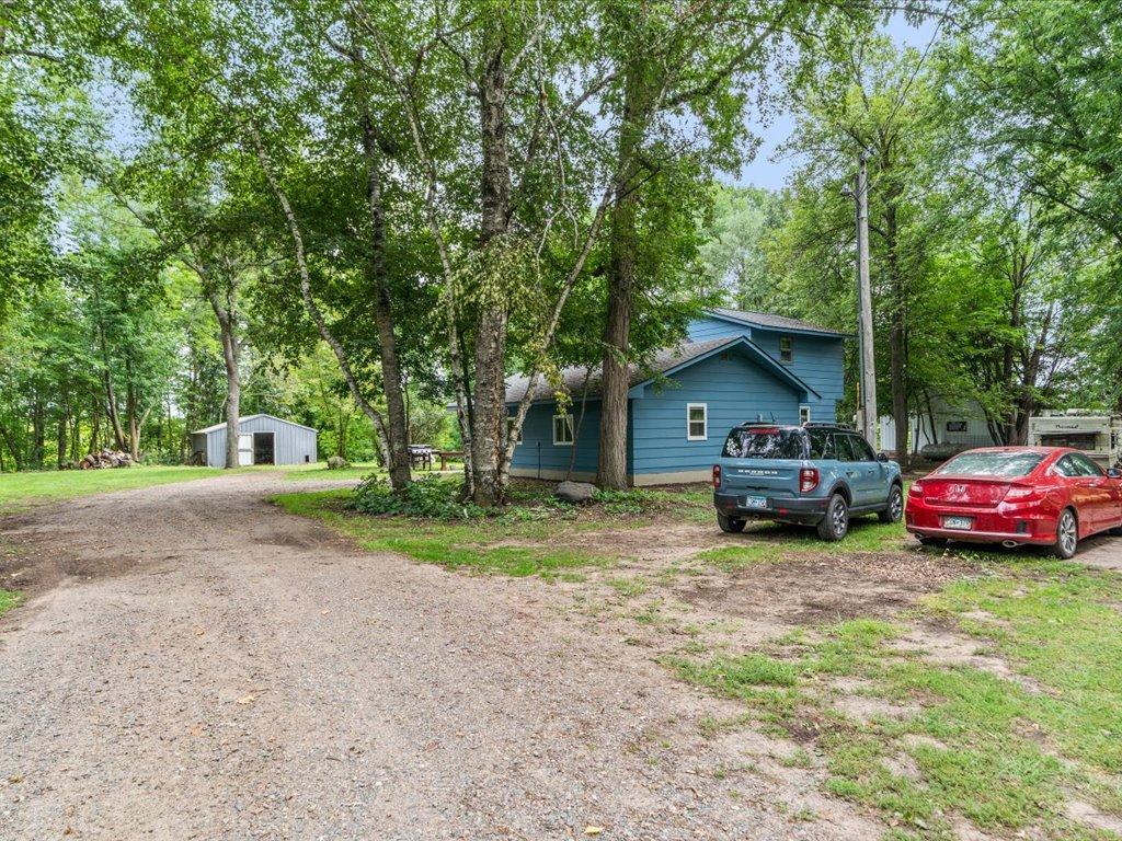 Blue house among mature trees beside a gravel driveway and detached garage.