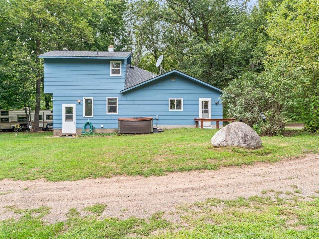 Blue two-story home with a satellite dish, wooded surroundings, and a large boulder in the yard.