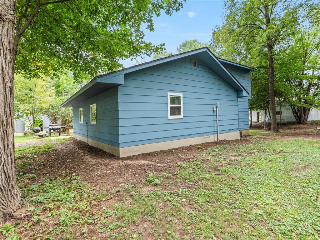 Blue-sided house surrounded by mature trees, viewed from its side and rear.