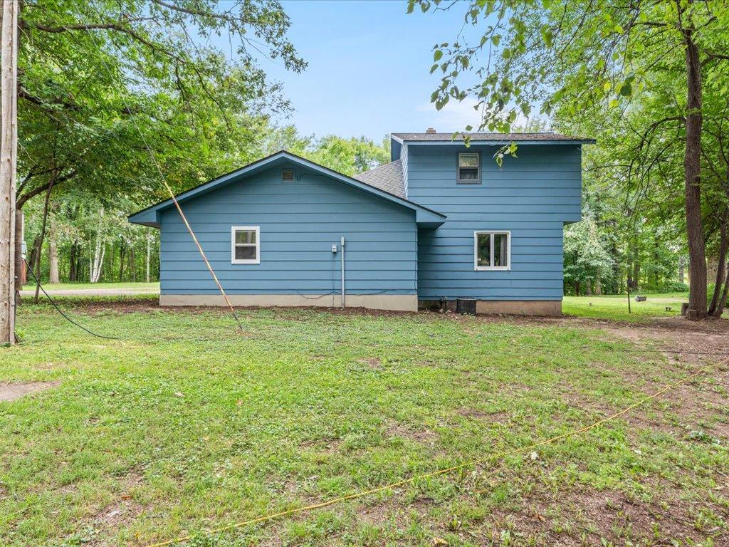 Blue two-story house surrounded by trees, viewed from the grassy side yard.