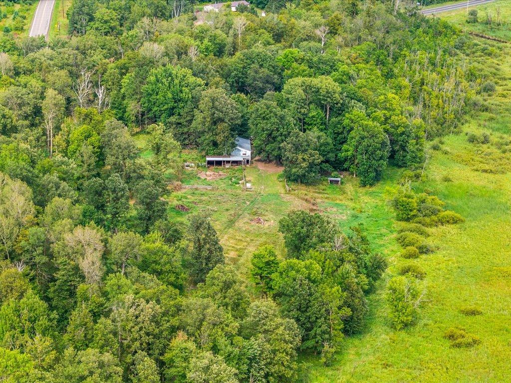 Aerial view of a small home in a wooded clearing beside open grassland.