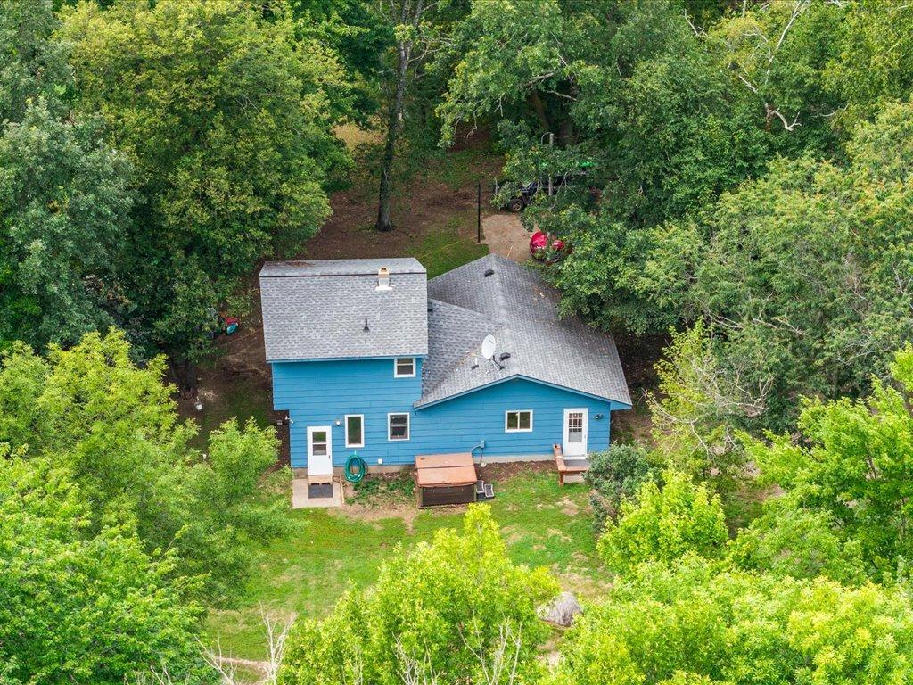 Blue house surrounded by dense trees, viewed from above with a grassy yard.