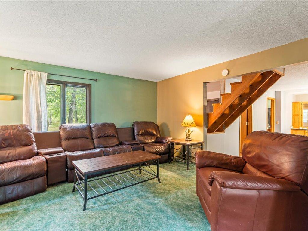 Living room with brown leather seating, green carpet, and a wooden staircase.