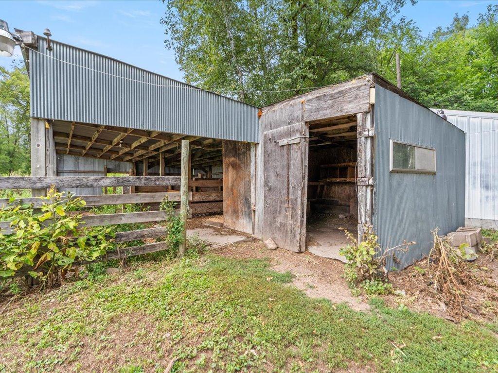 Weathered wooden barn with open livestock pens beside a corrugated metal shed.