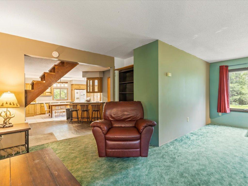 Living room with a leather recliner, green carpet, and open view to the kitchen and staircase.