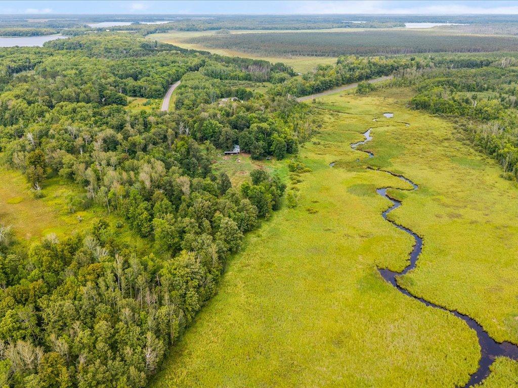 Aerial view of wooded acreage and wetlands with a winding creek, road, and small outbuilding.