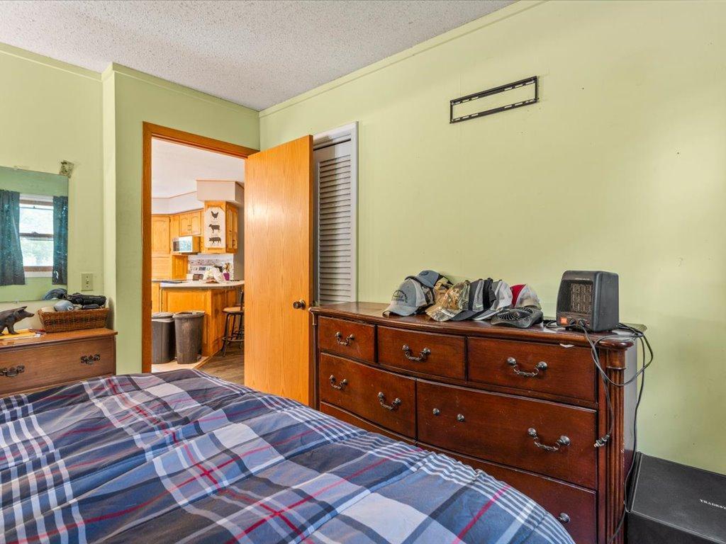 Bedroom with a plaid bedspread, wooden dresser, and open doorway to the kitchen.