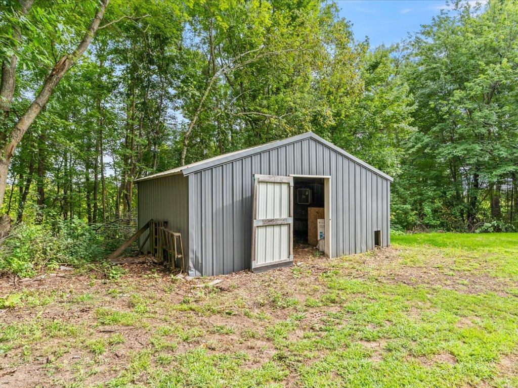 Gray metal outbuilding with an open door in a wooded clearing.