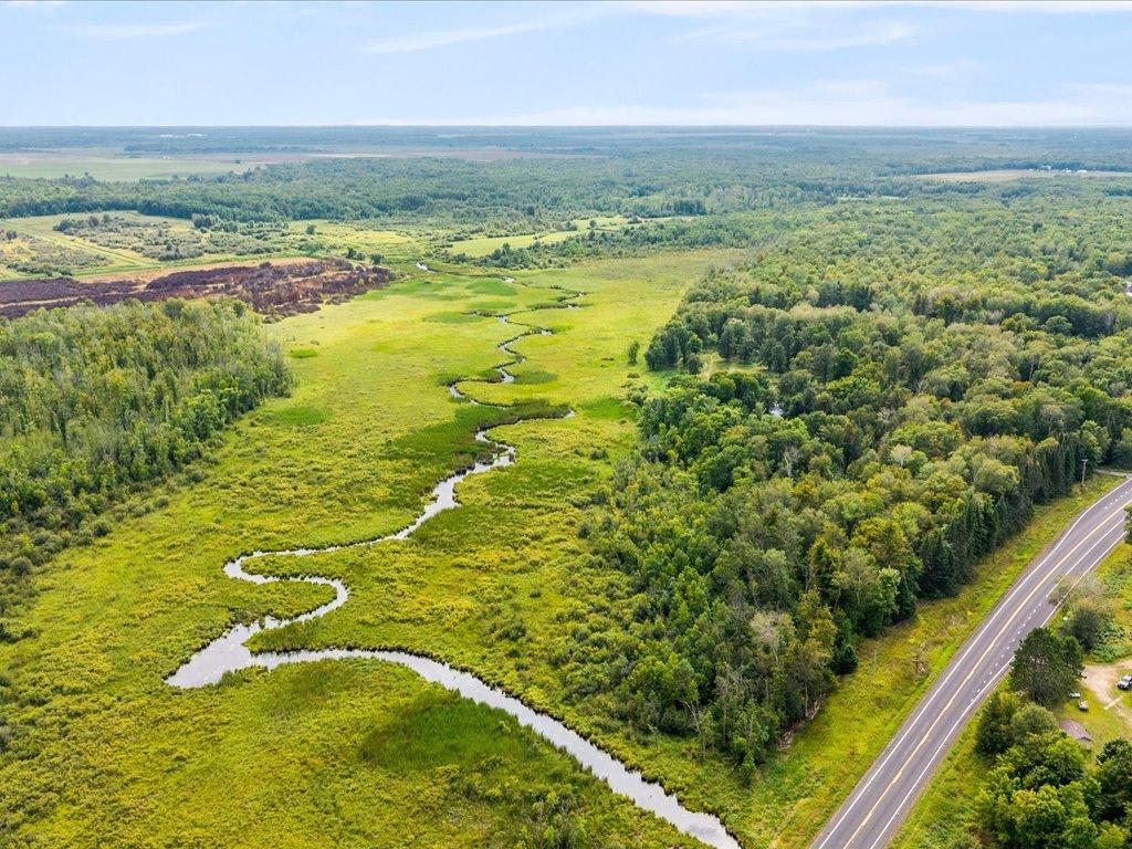 Aerial view of wooded wetlands and a winding creek beside State Highway 210.