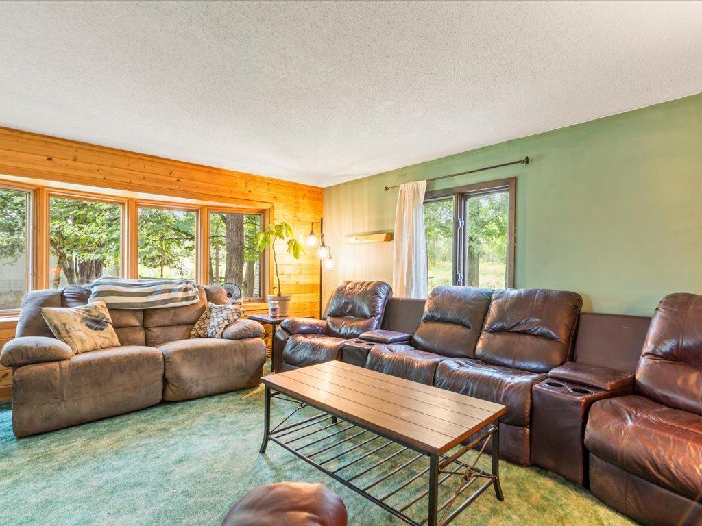 Living room with leather sofas, a wood-paneled wall, and large windows overlooking trees.