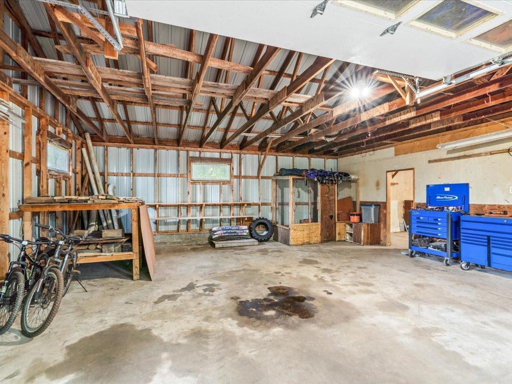 Spacious garage workshop with exposed timber trusses, bicycles, shelving, and blue rolling tool chests.
