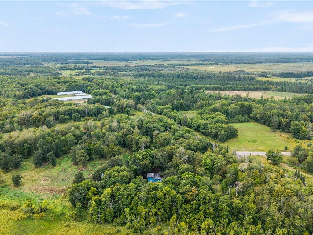 Aerial view of wooded acreage with open fields and a small blue-roofed home.