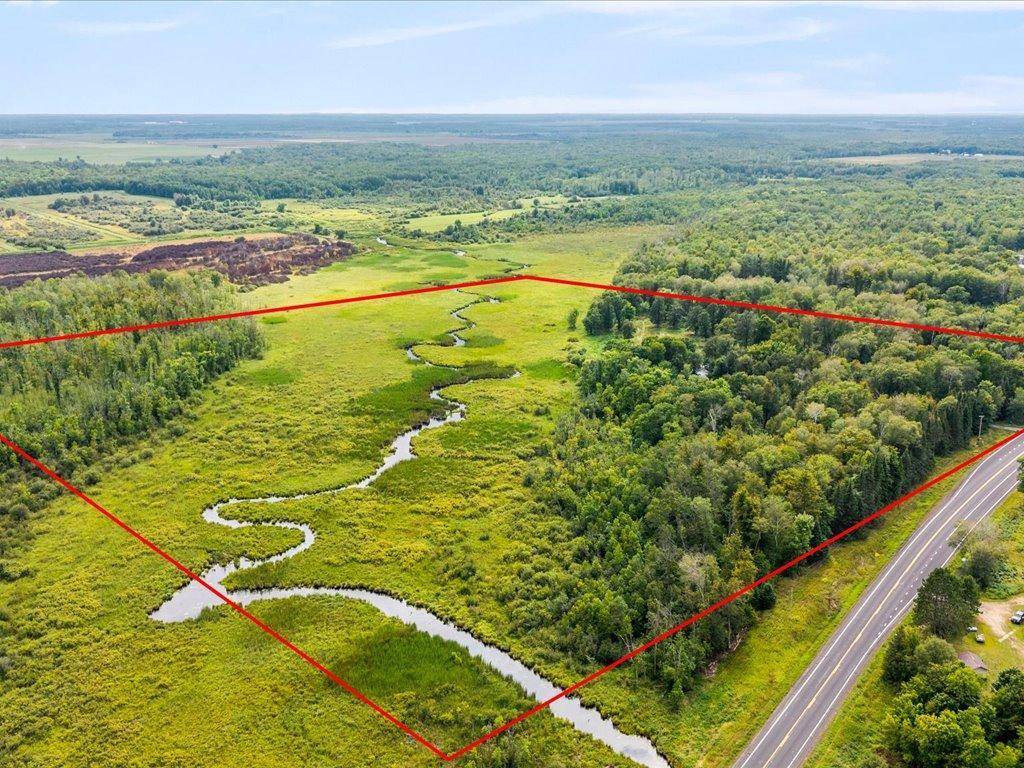 Aerial view of a wetland property with a winding creek, wooded edges, and highway frontage.
