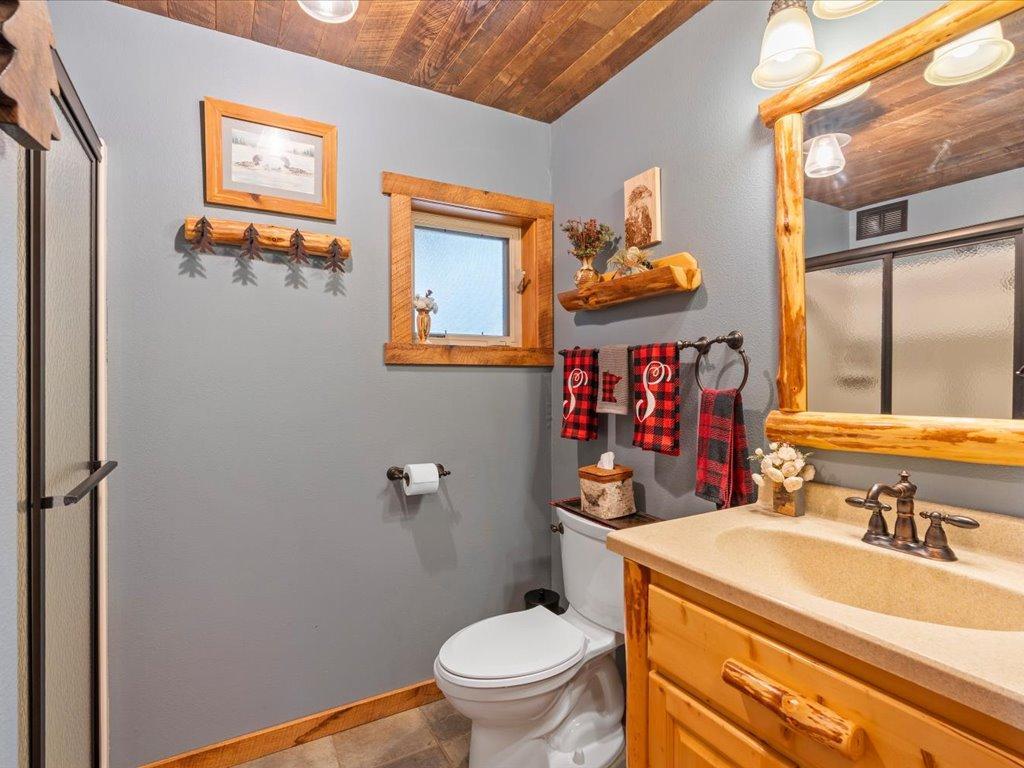 Rustic bathroom with log-style wood trim, a tan vanity, white toilet, and glass shower enclosure.