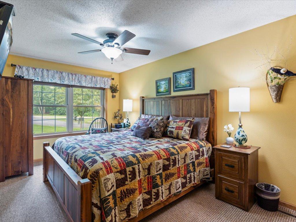 Bedroom with a wooden bed, colorful patchwork quilt, and wide window overlooking a green yard.