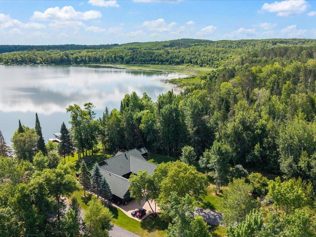 Aerial view of a tree-surrounded home near a calm lake and wooded shoreline.