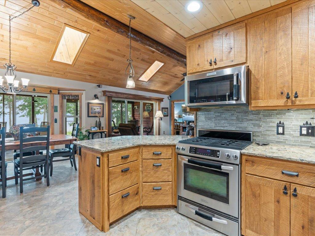 Kitchen with a granite island, wood cabinets, stainless steel appliances, and a vaulted wood ceiling.