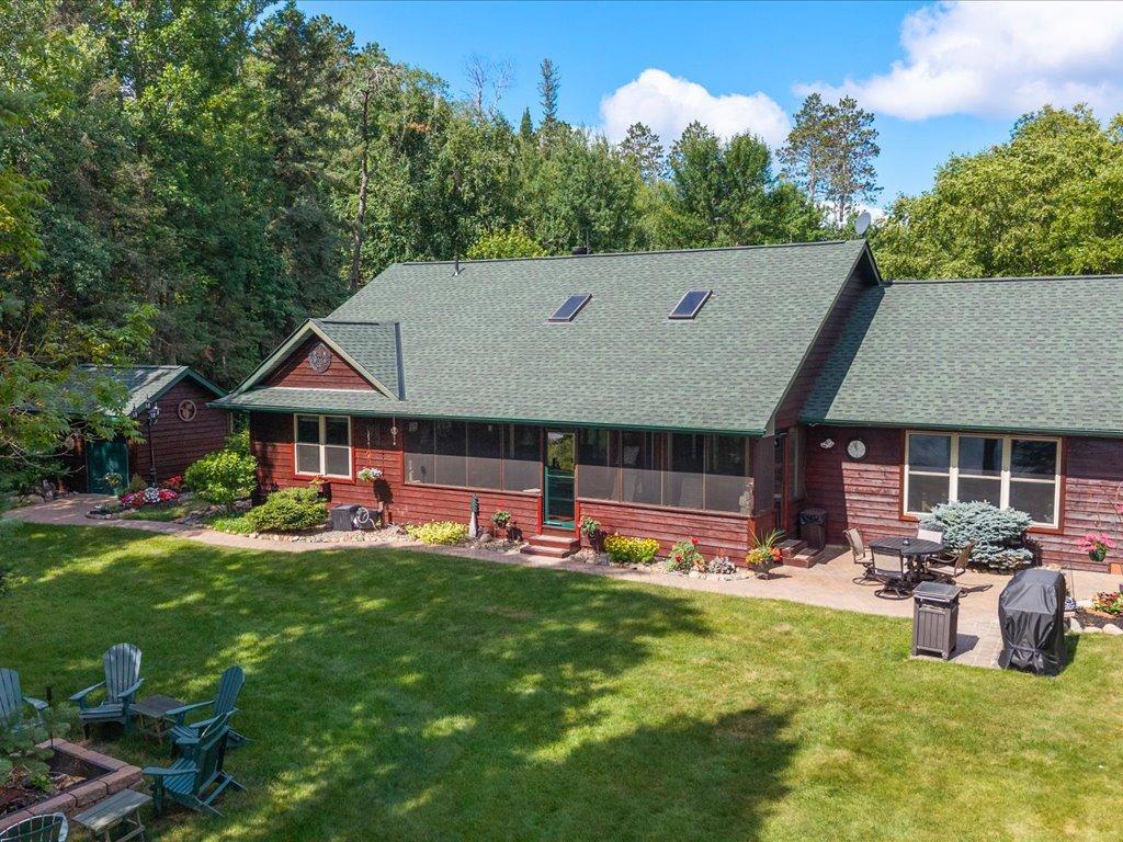 Red-sided home with a long screened porch, patio seating, and a wooded backdrop.