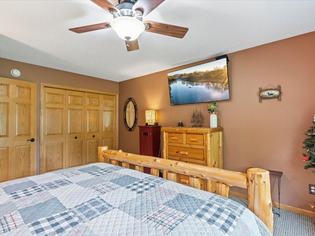 Bedroom with a log-style wooden bed, blue plaid quilt, pine dresser, and ceiling fan.