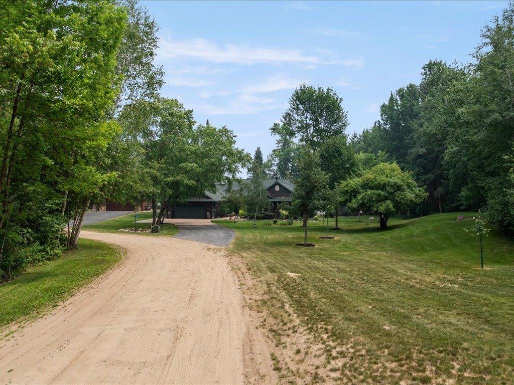 Home among mature trees, viewed from a curving sandy driveway across a broad lawn.