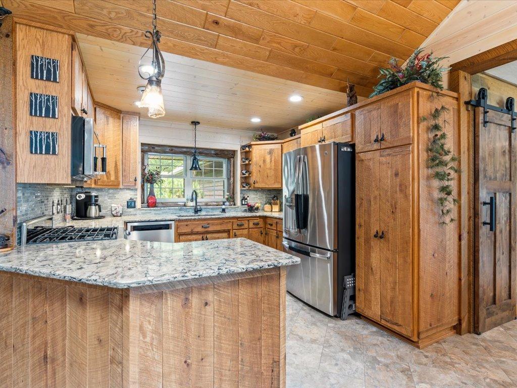 Rustic kitchen with a large granite island, warm wood cabinetry, and stainless steel refrigerator.