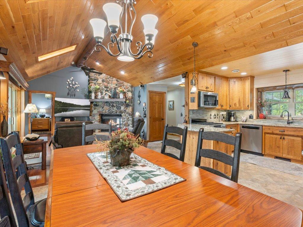 Open-plan dining and living area with a vaulted wood ceiling and stone fireplace.