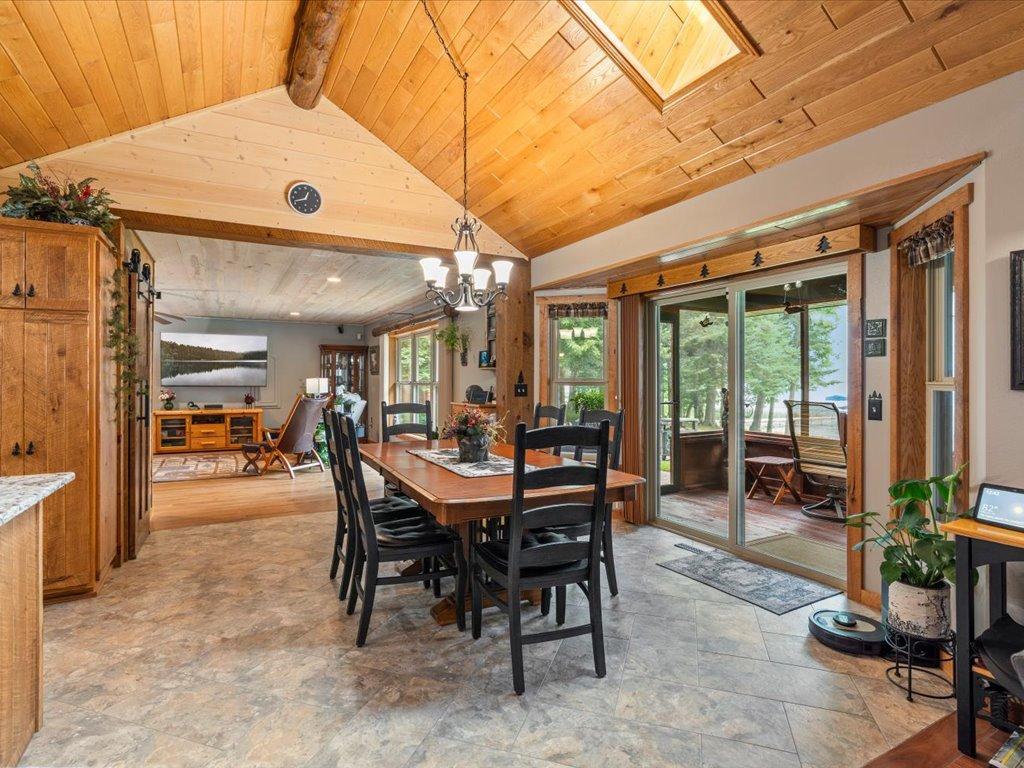 Dining area with a vaulted wood ceiling, long table, and sliding glass doors overlooking the lake.