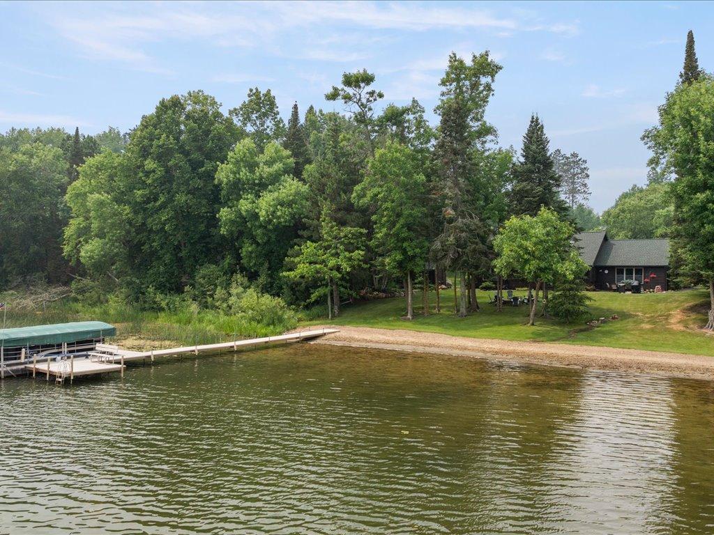 Lakeside cabin among mature trees, with a covered dock and wooden pier extending into the water.